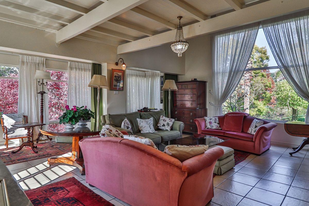 Spacious living room featuring exposed timber ceiling beams, large windows with garden views, and tiled flooring, creating a bright and inviting atmosphere.