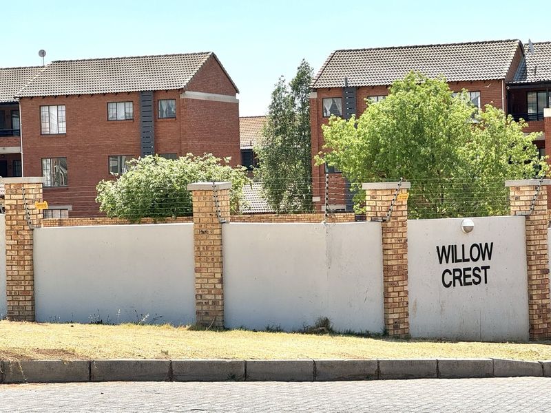 Exterior view of the Willow Crest apartment complex featuring a brick boundary wall with electric fencing and complex signage.