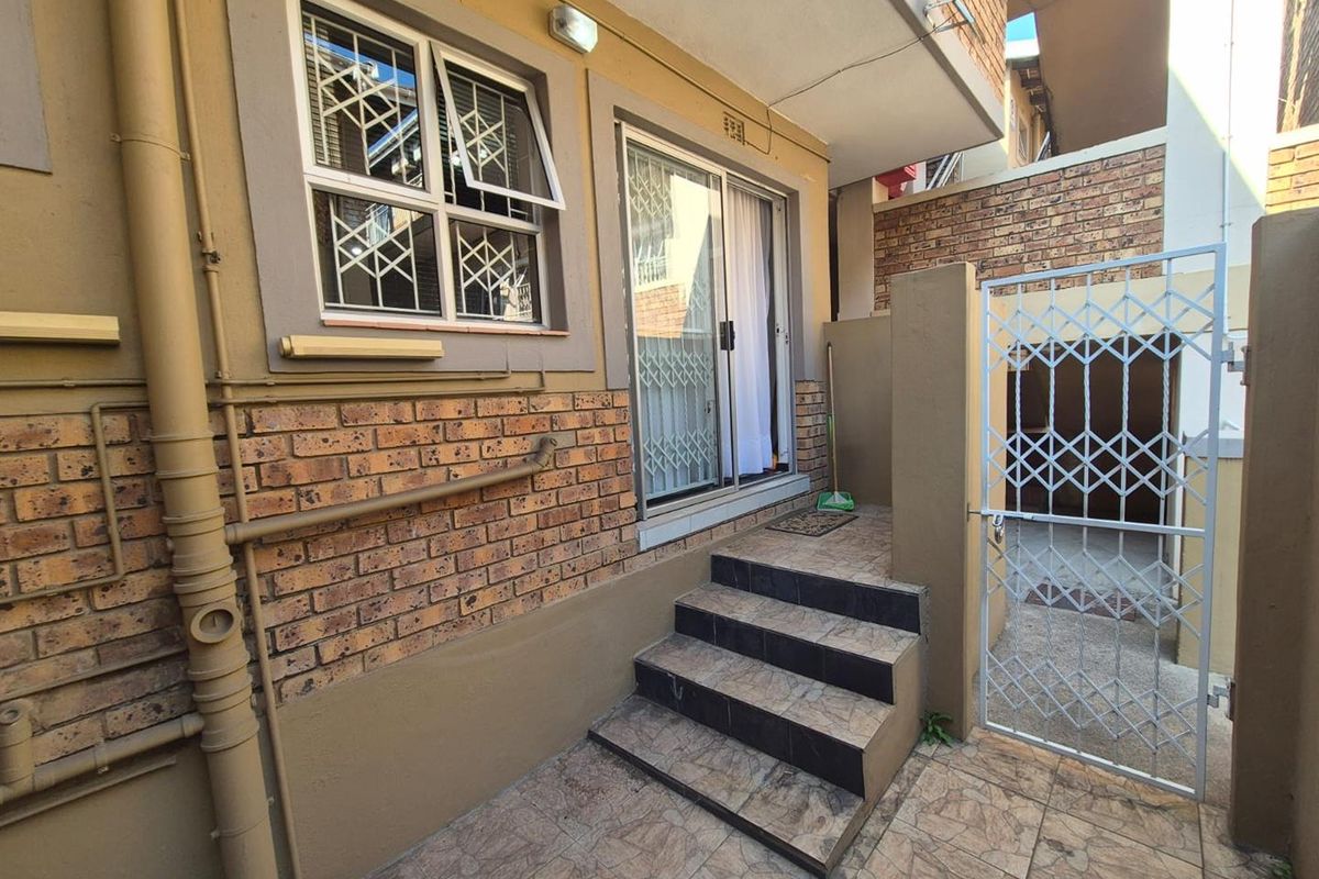 Rear exterior view of the apartment featuring a tiled patio, access steps, sliding glass door, and security gates.