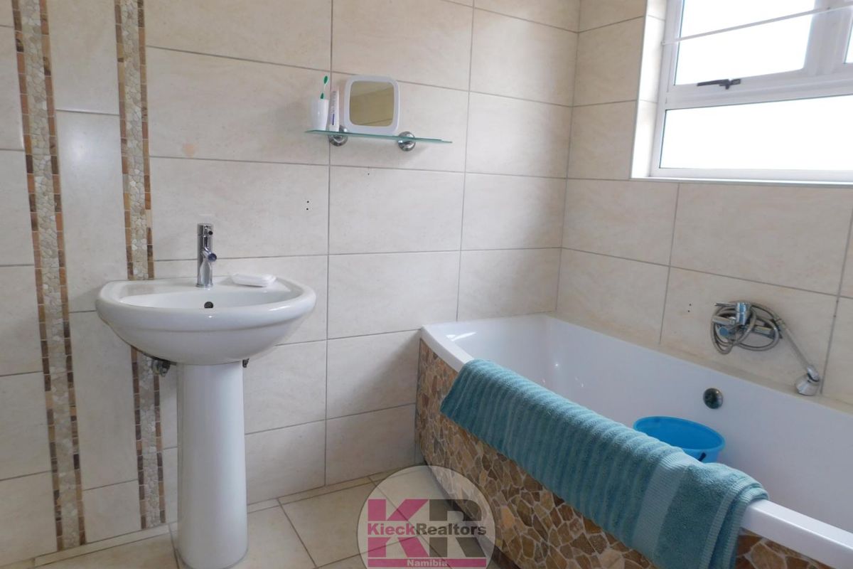 A functional bathroom featuring a pedestal basin, bathtub with mosaic tile detailing, and neutral wall tiling.