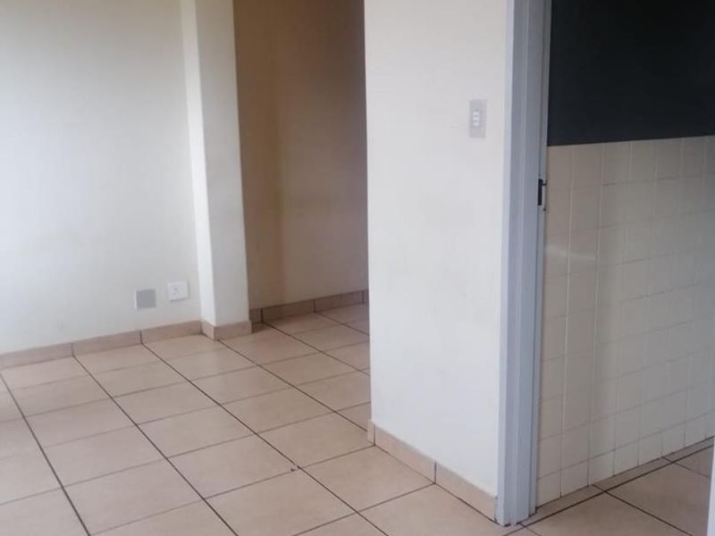 An empty living area featuring neutral ceramic floor tiles and a doorway leading to an adjacent space with tiled wall finishes.