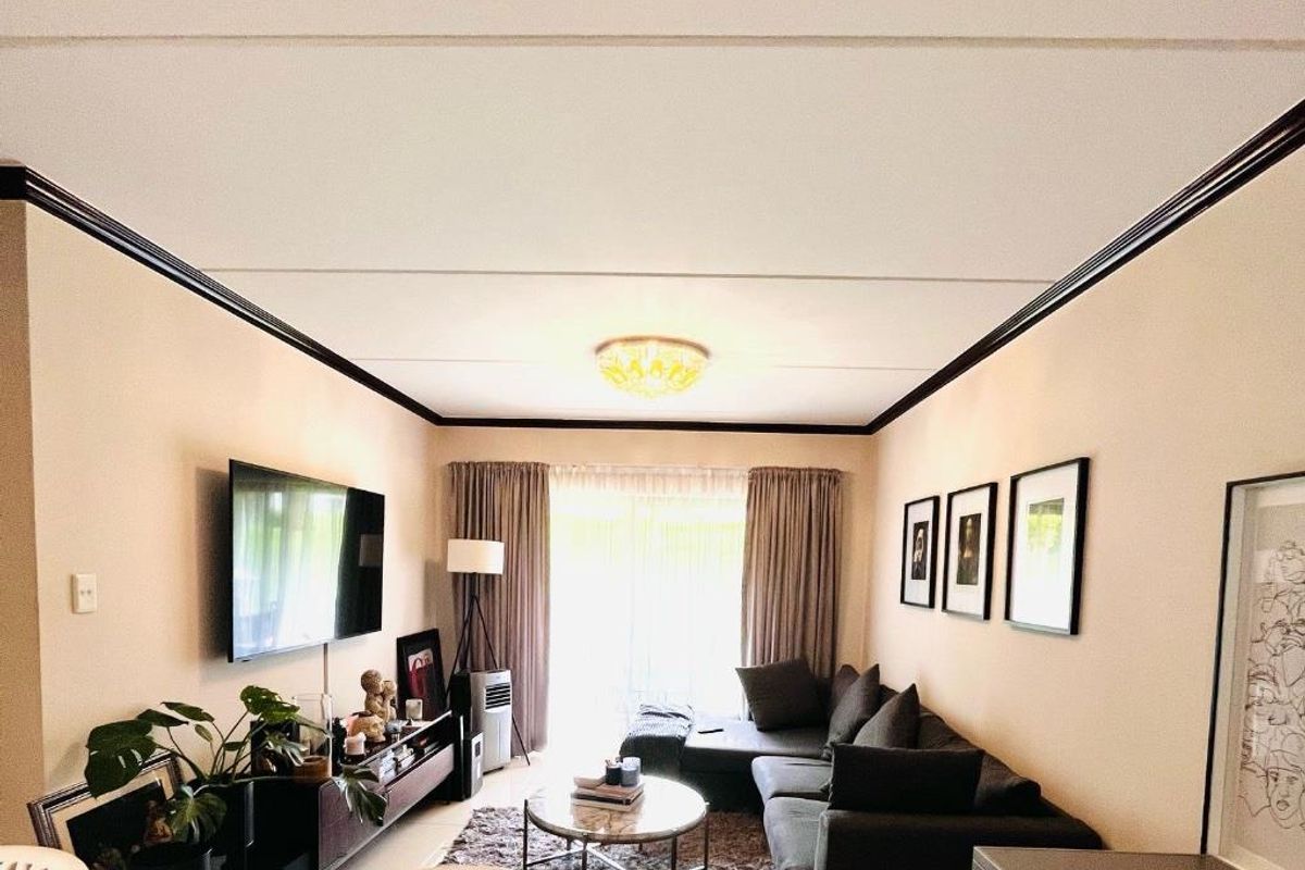 A comfortable living room featuring a ceiling cornice, central lighting, and a sliding glass door providing access to the exterior.