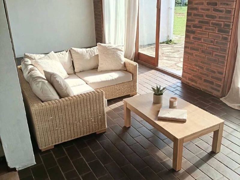 A covered patio area featuring exposed brick walls, timber ceiling, and tiled flooring, with direct access to the garden through sliding glass doors.
