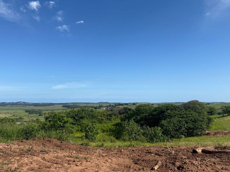 A scenic, elevated view overlooking expansive green fields, rolling hills, and natural vegetation on a vacant residential plot.