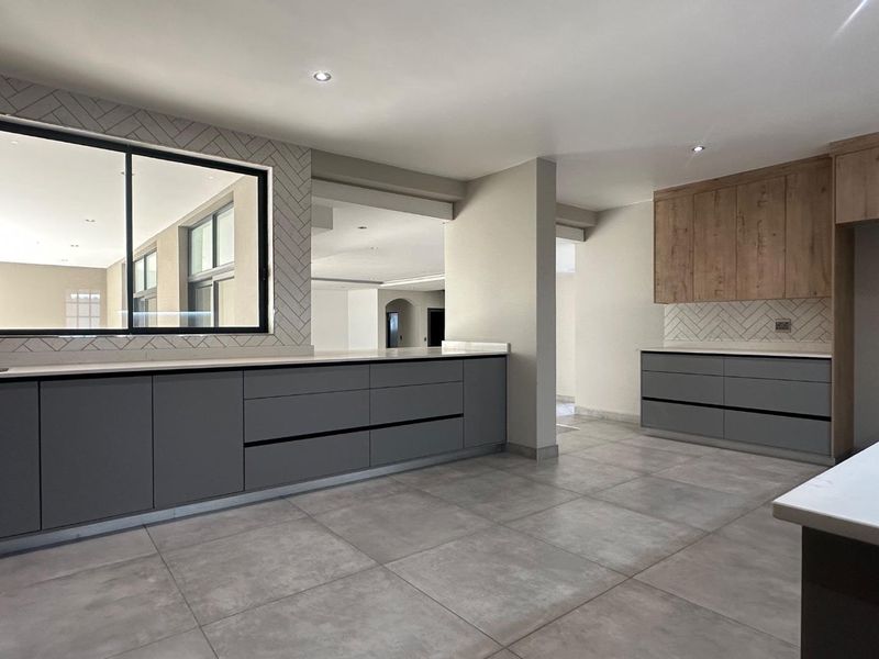 Modern kitchen featuring sleek grey cabinetry, timber-look overhead units, stone countertops, and a stylish herringbone tile splashback with large format floor tiles.