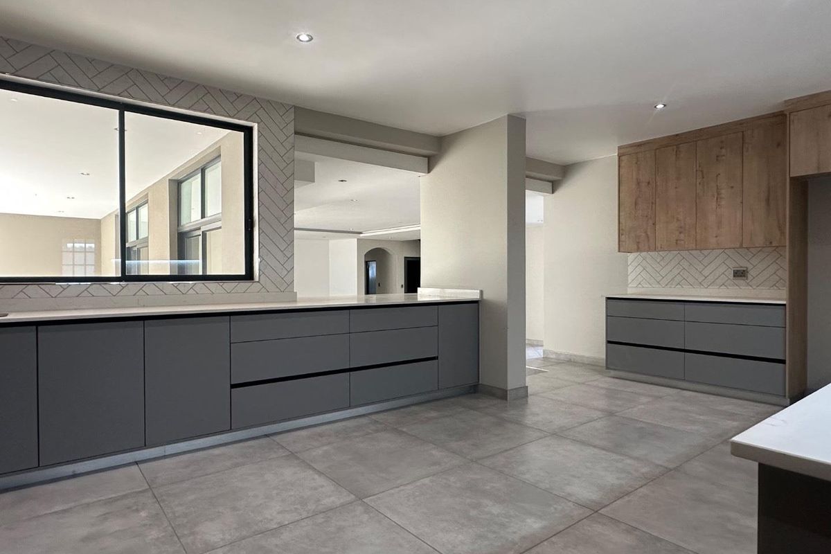 Modern kitchen featuring sleek grey cabinetry, timber-look overhead units, stone countertops, and a stylish herringbone tile splashback with large format floor tiles.