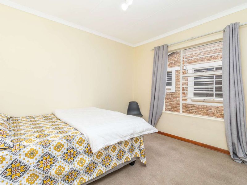 A functional bedroom featuring neutral wall tones, carpeted flooring, and a window fitted with security bars.