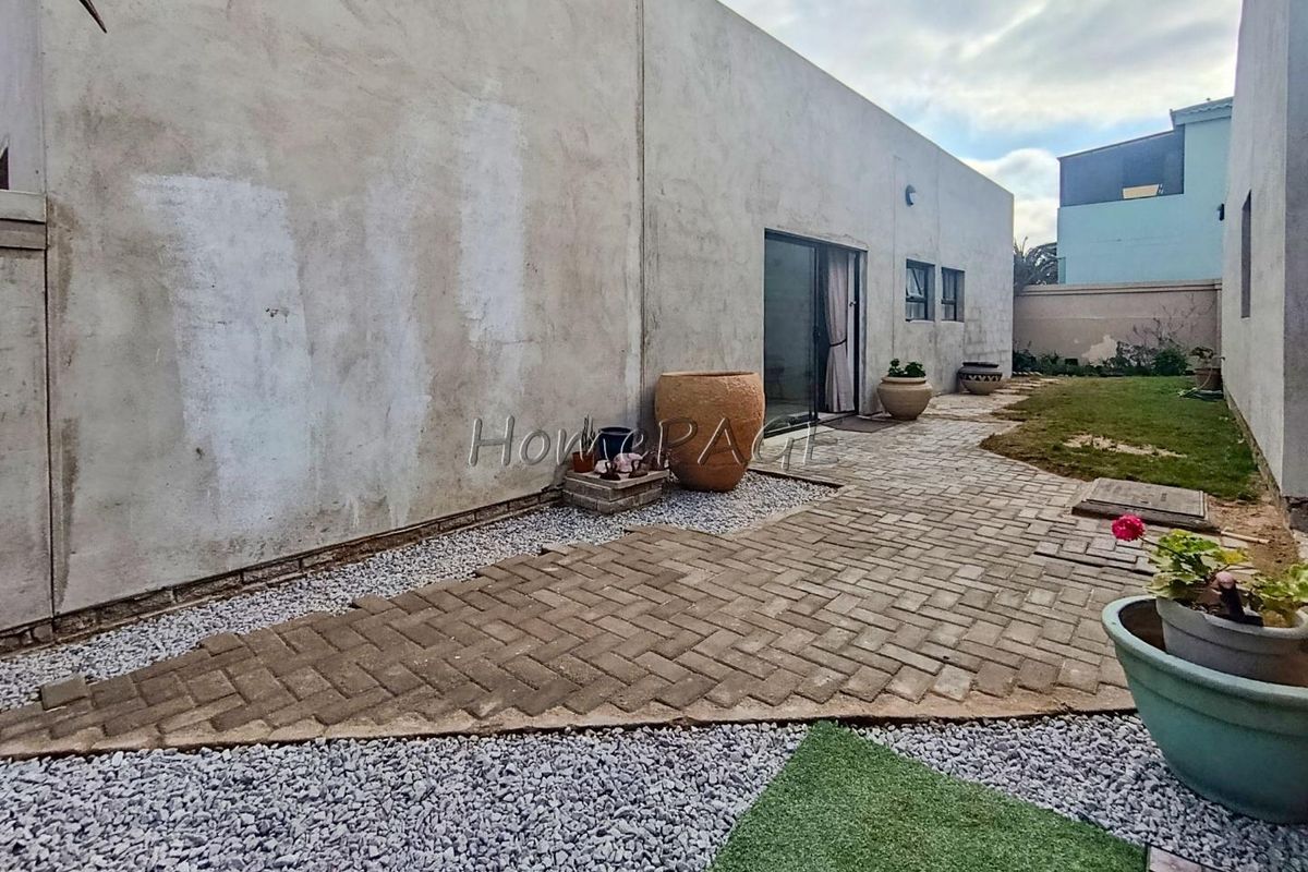 Rear exterior view featuring a paved patio area, gravel landscaping, and an unfinished concrete wall surface leading to a sliding glass door entrance.