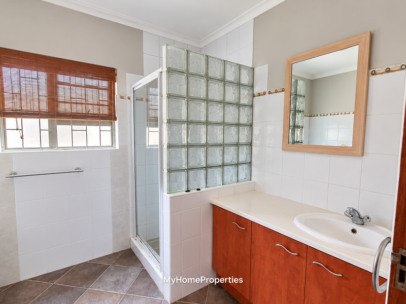 A functional bathroom featuring a glass block shower partition, built-in vanity with basin, and neutral wall tiling.