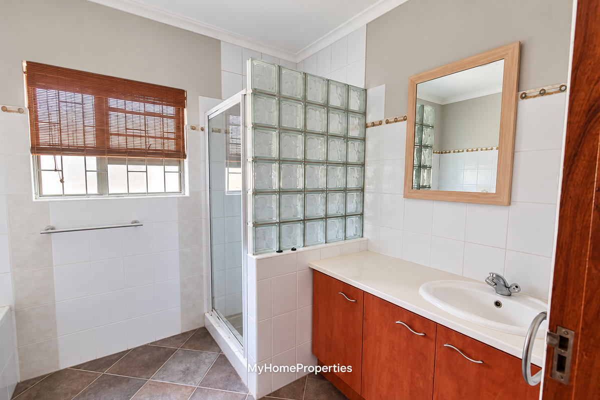 A functional bathroom featuring a glass block shower partition, built-in vanity with basin, and neutral wall tiling.