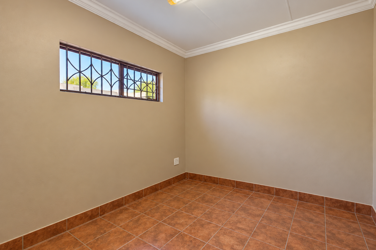 A clean, empty bedroom featuring neutral wall paint, durable ceramic floor tiles, and a high-level window with security bars.