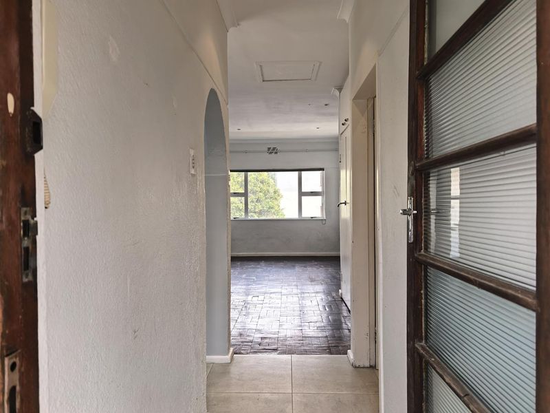 A vacant hallway featuring a mix of tiled and parquet flooring, leading through an arched doorway into an open living area with natural light.