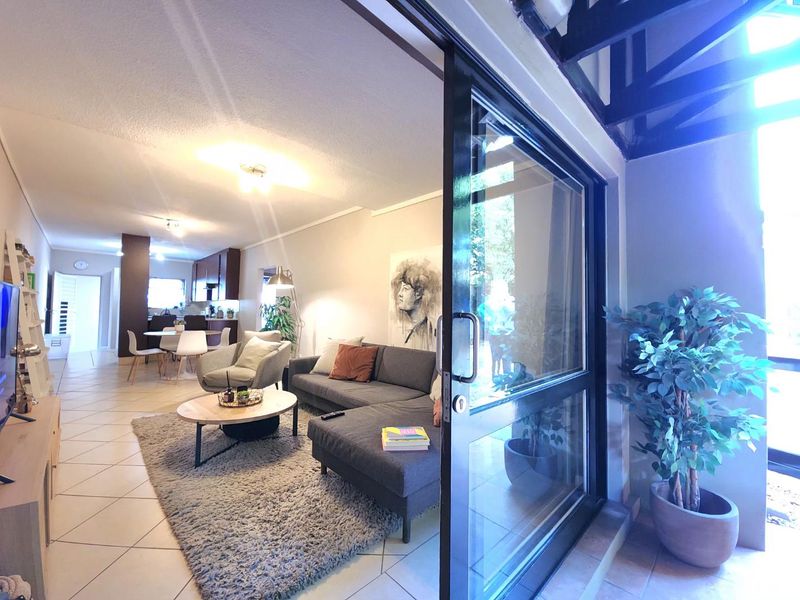 Open-plan living and dining area featuring tiled floors, exposed ceiling beams, and a large sliding glass door leading to an outdoor space.