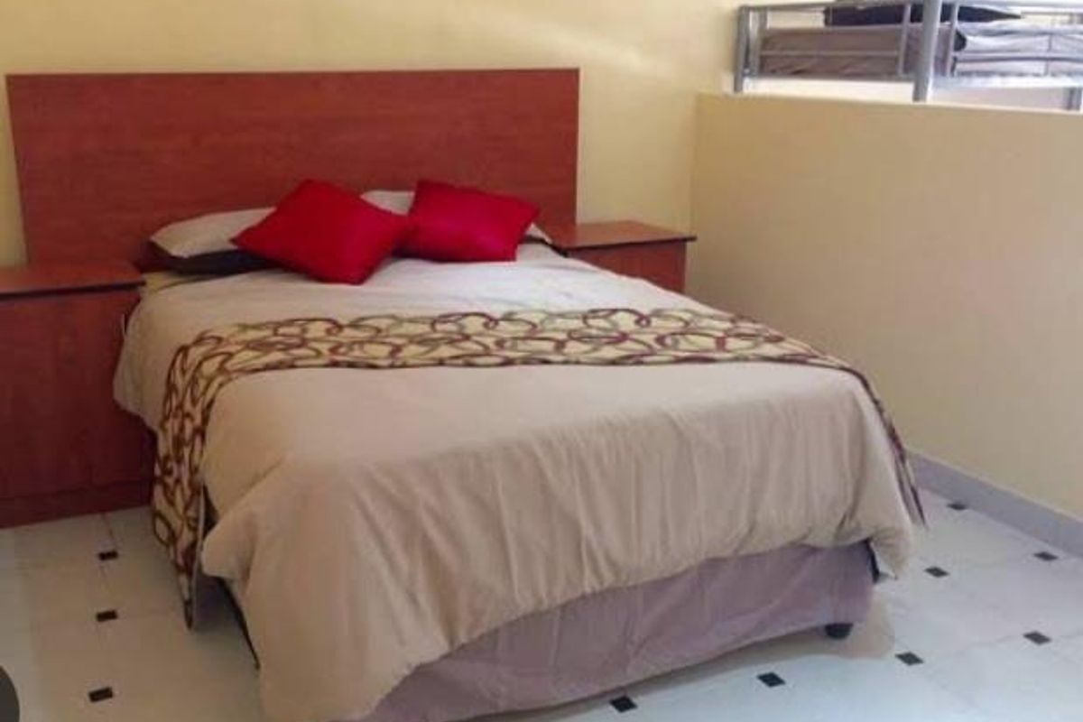 A bedroom featuring a built-in wooden headboard and matching bedside pedestals, finished with tiled flooring.