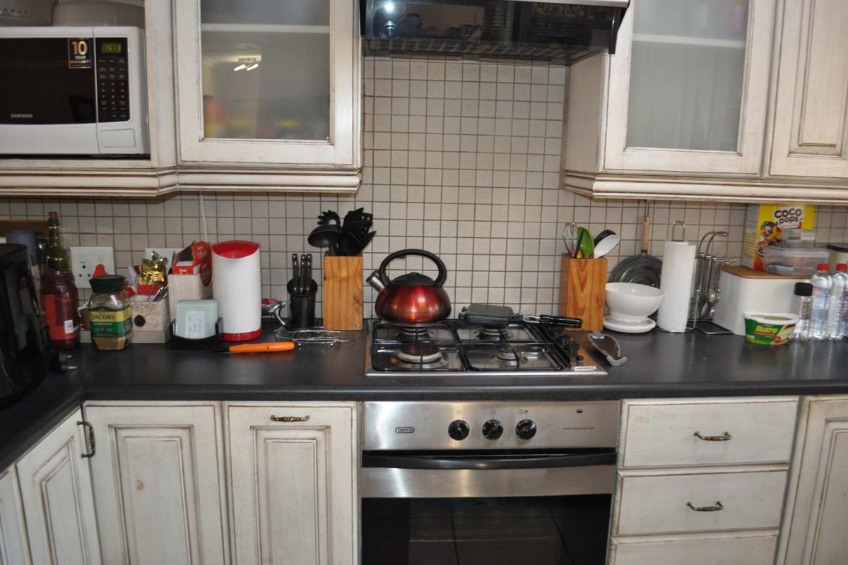 A kitchen workspace featuring a gas hob, built-in oven, extractor fan, and integrated microwave with tiled backsplash and traditional cabinetry.