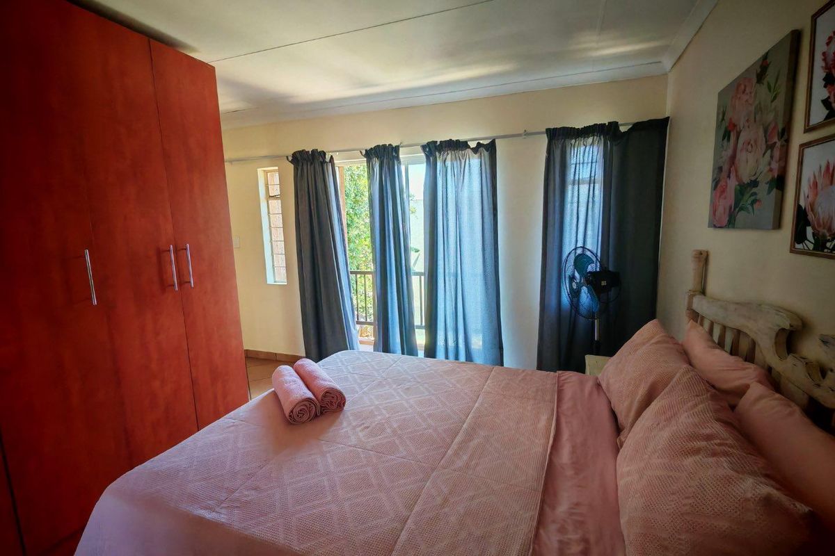 A comfortable bedroom featuring built-in wooden wardrobes and large windows with access to a balcony, providing natural light and ventilation.