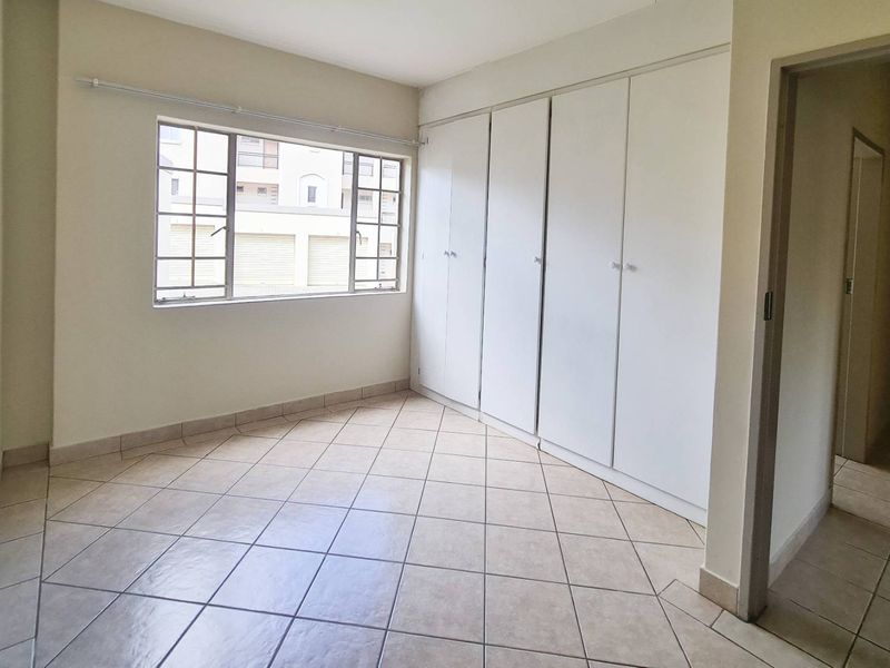 A bright, empty bedroom featuring neutral tiled flooring and ample built-in cupboard storage space.
