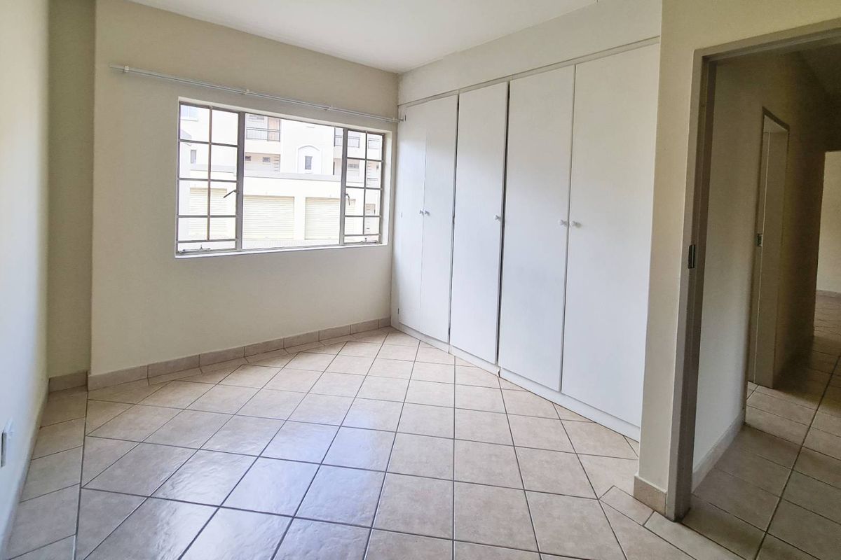 A bright, empty bedroom featuring neutral tiled flooring and ample built-in cupboard storage space.