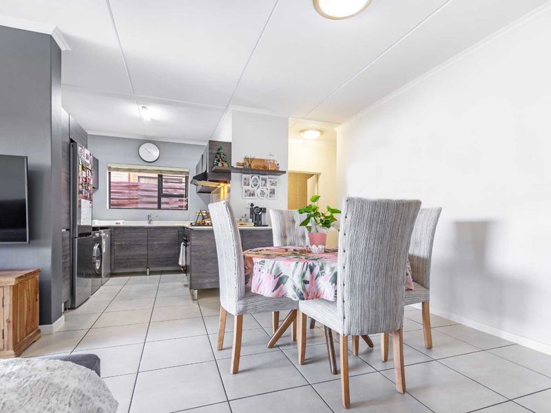An open-plan living and dining area featuring tiled flooring, a modern kitchen with built-in cabinetry, and integrated appliances.