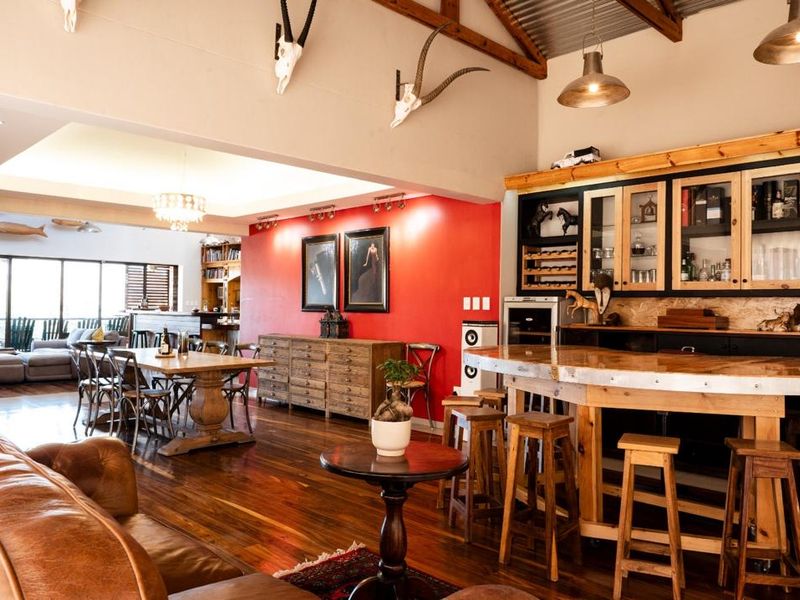 Spacious open-plan living and entertainment area featuring a built-in wooden bar, exposed timber roof trusses, and polished hardwood flooring.