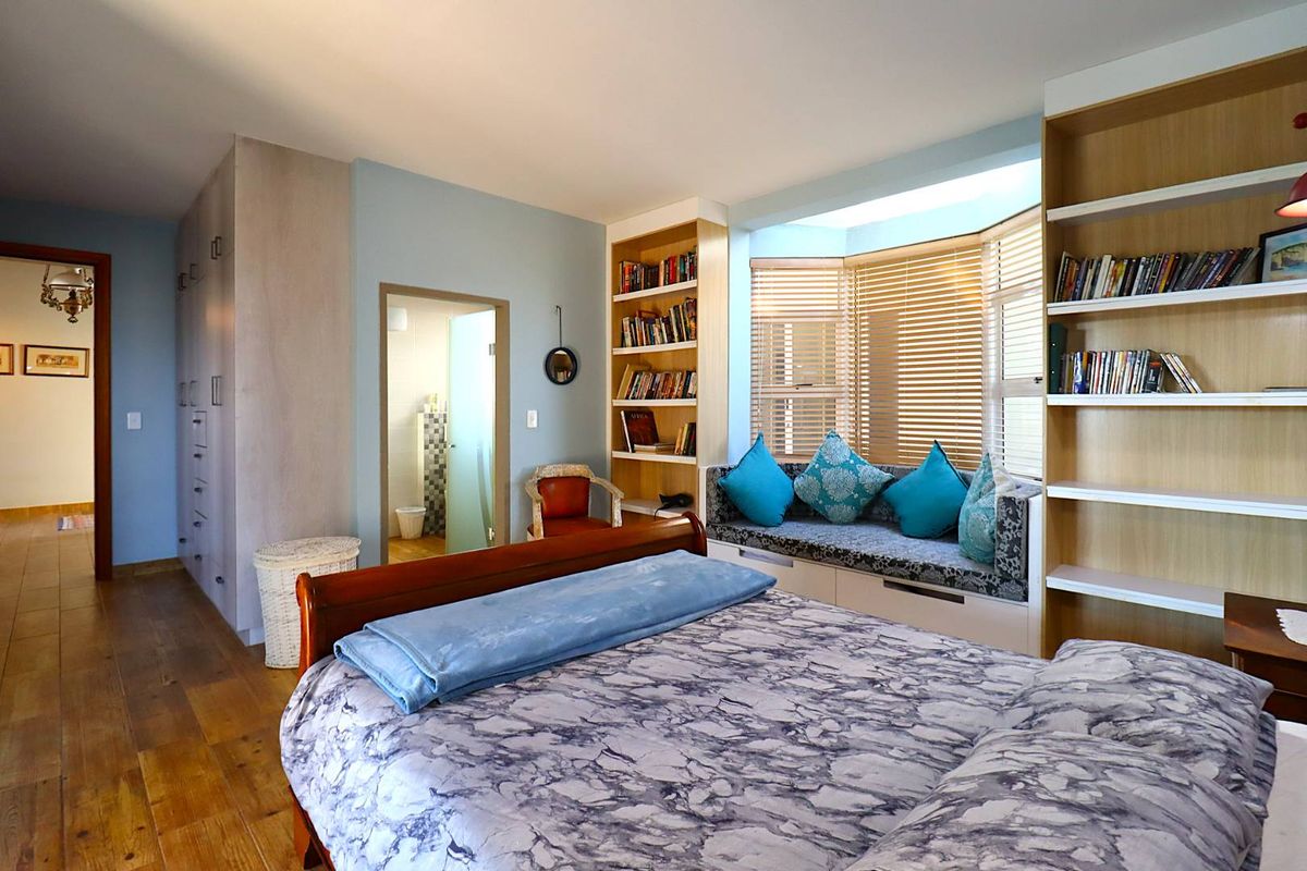 A well-lit bedroom featuring built-in floor-to-ceiling cabinetry, integrated shelving, and a cozy bay window seat with wooden blinds.