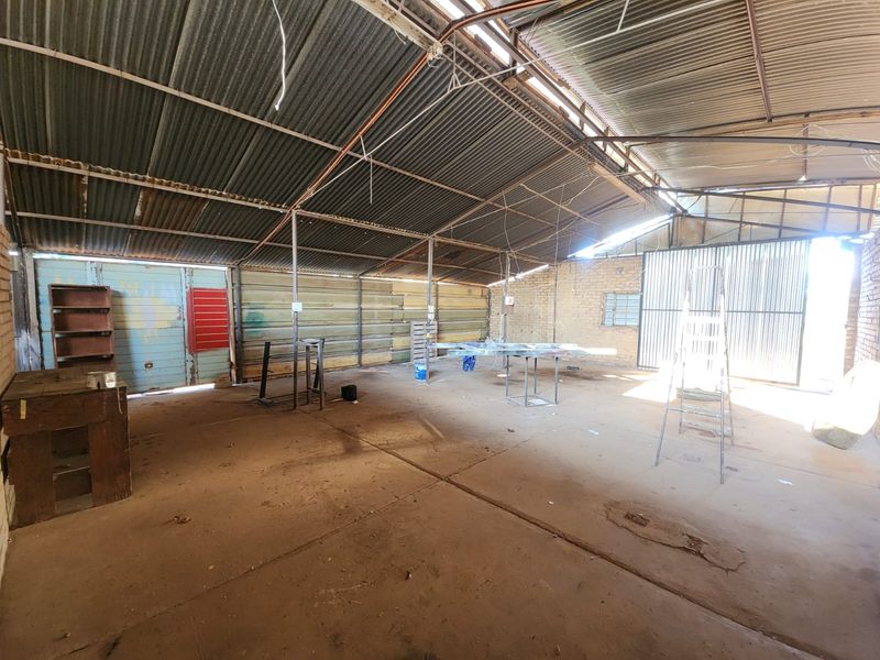 A spacious, industrial-style garage or workshop featuring a corrugated metal roof, exposed steel structure, and concrete flooring, suitable for storage or renovation.