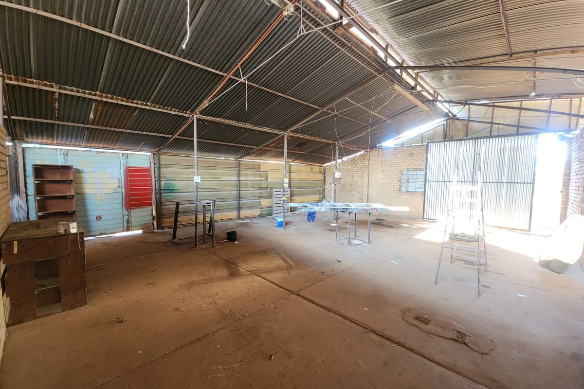 A spacious, industrial-style garage or workshop featuring a corrugated metal roof, exposed steel structure, and concrete flooring, suitable for storage or renovation.