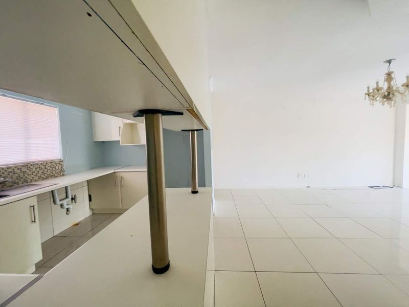An open-plan living and kitchen area featuring tiled flooring, a breakfast bar, and a neutral color palette, ready for personalization.