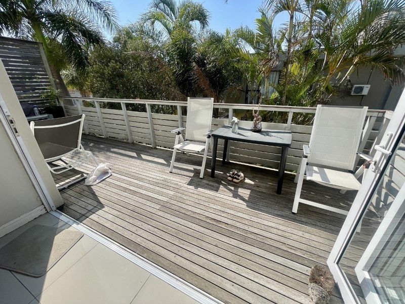 A private balcony featuring timber decking and a slatted balustrade, accessible via sliding glass doors, offering an outdoor space for relaxation.