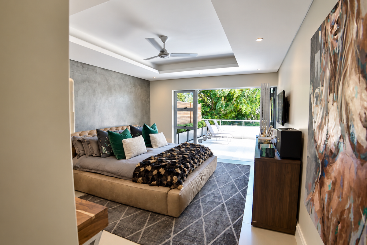 Spacious modern bedroom featuring a tray ceiling, recessed lighting, a feature wall, and large sliding glass doors opening onto a private balcony.