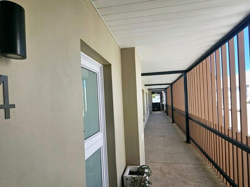A clean, covered exterior walkway featuring modern metal slat privacy screening and wall-mounted lighting, providing access to apartment unit number four.
