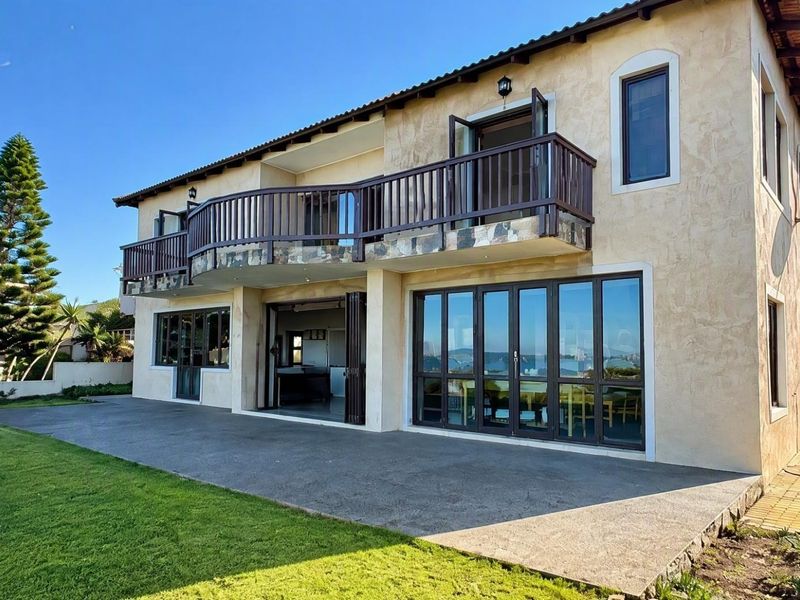 Rear view of a two-story house featuring a spacious concrete patio, a large balcony with stone detailing, and expansive folding glass doors.