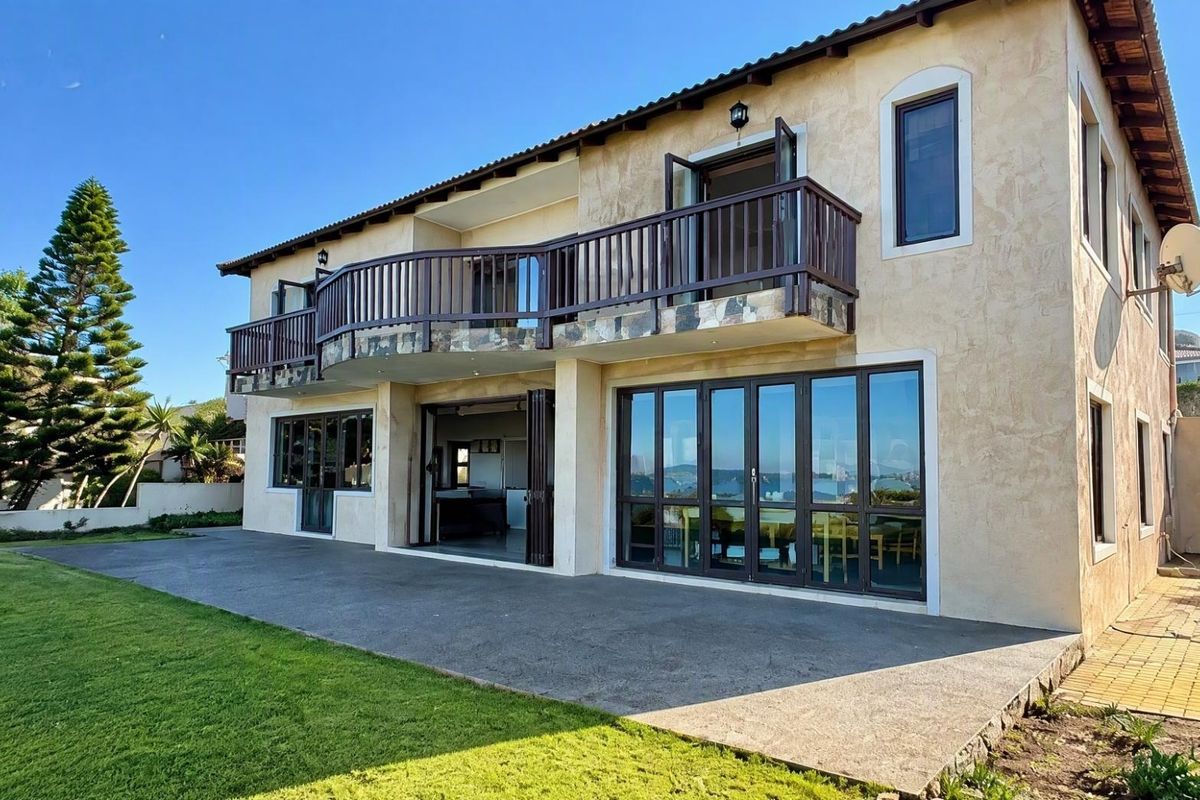 Rear view of a two-story house featuring a spacious concrete patio, a large balcony with stone detailing, and expansive folding glass doors.