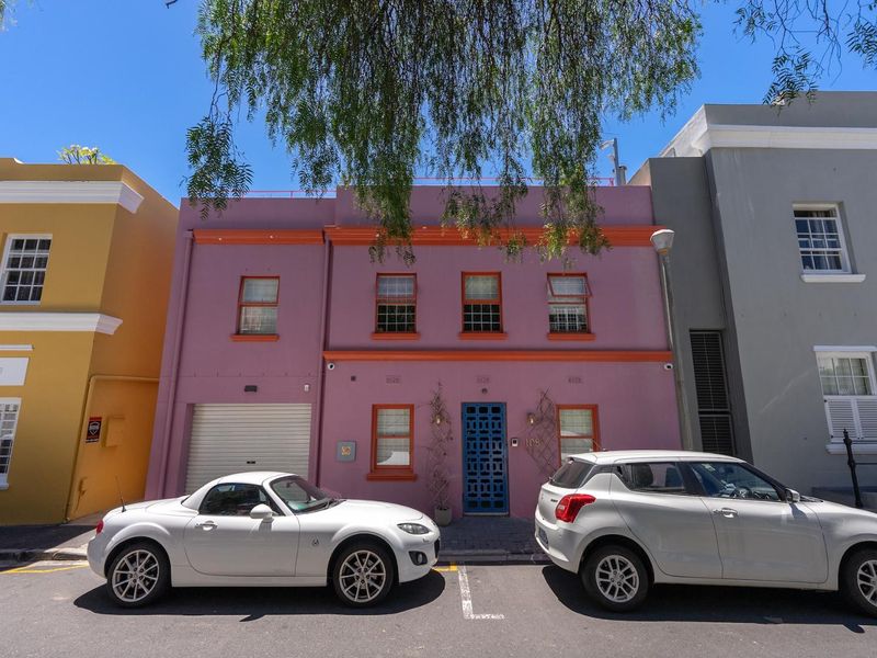 Front elevation of a two-story townhouse featuring a distinctive pink facade, orange trim, integrated garage, and secure entrance.