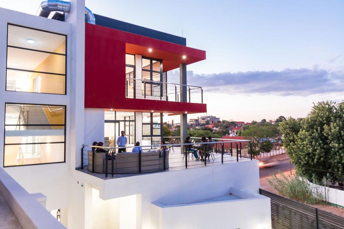 Modern multi-story hotel exterior featuring a spacious elevated balcony with metal railings and large glass windows overlooking the surrounding area.
