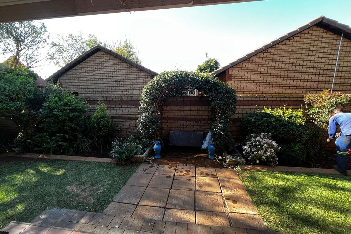 A rear garden area featuring a paved walkway, brick boundary walls, and a decorative metal garden archway.