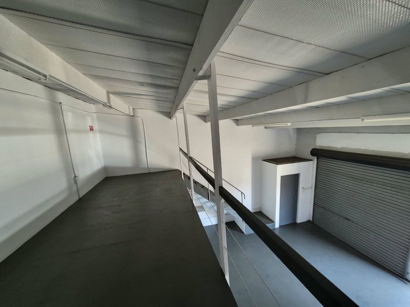 An industrial mezzanine level featuring exposed steel beams, a metal roller shutter door, and functional lighting, suitable for storage or workspace.