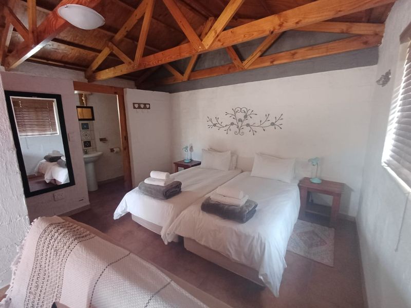 A rustic bedroom featuring exposed timber roof trusses, tiled flooring, and an attached en-suite bathroom with a pedestal basin.