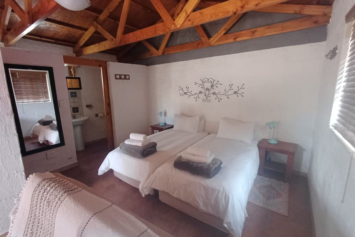 A rustic bedroom featuring exposed timber roof trusses, tiled flooring, and an attached en-suite bathroom with a pedestal basin.