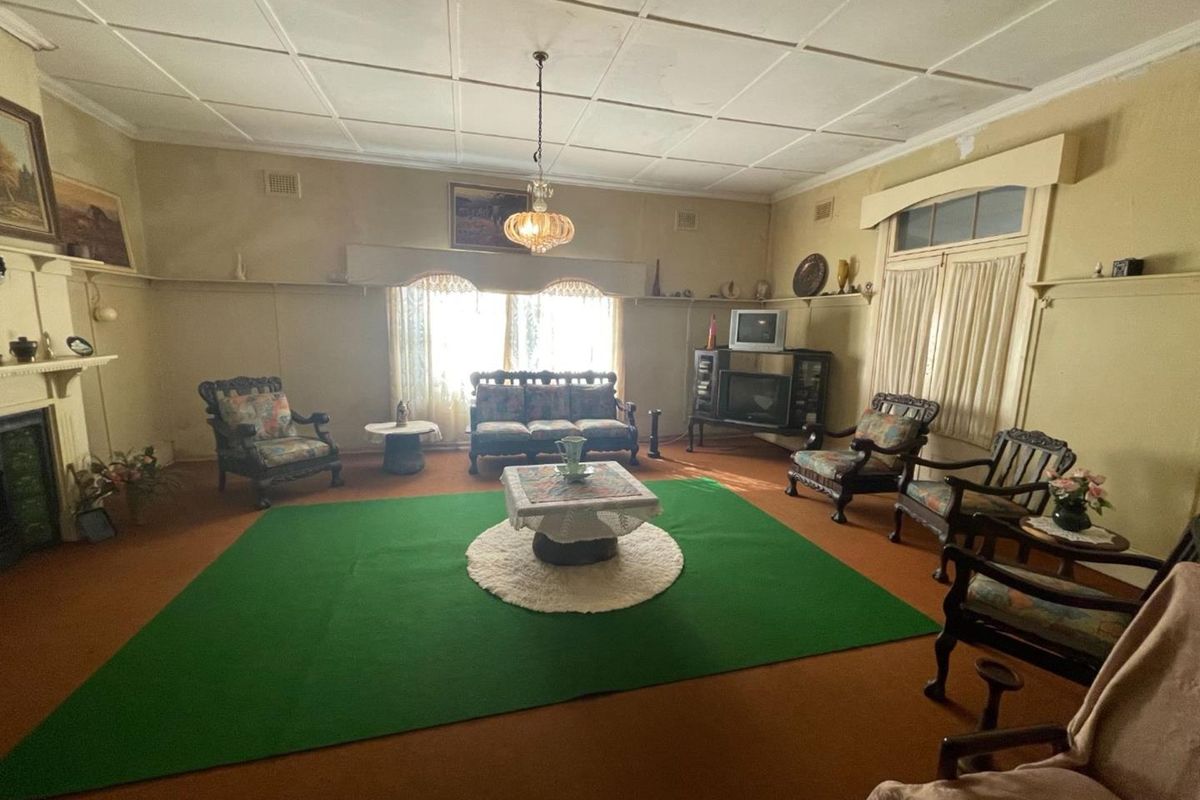 A spacious, vintage-style living room featuring a fireplace, traditional ceiling tiles, and large windows allowing for natural light.
