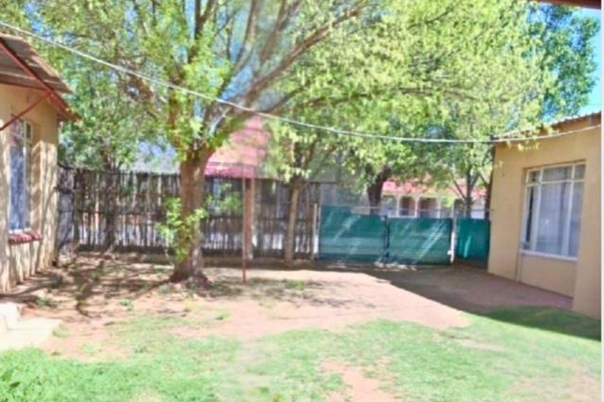 A private rear garden area featuring mature trees, perimeter fencing, and direct access to the main dwelling structures.