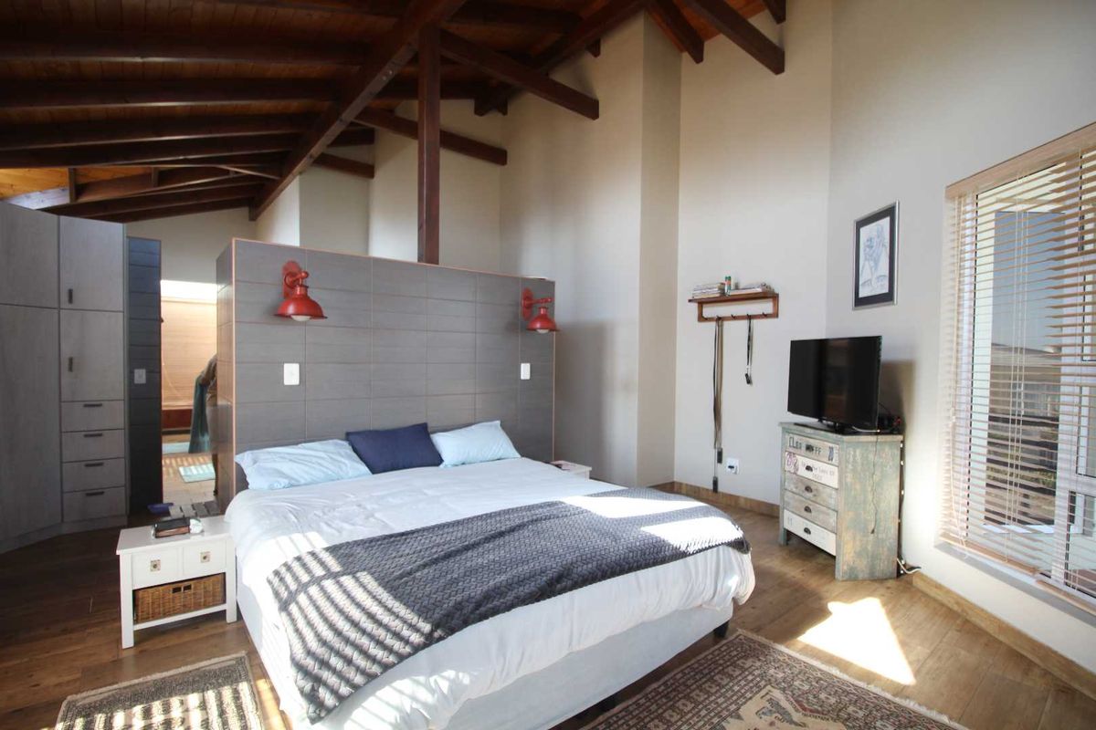 Spacious bedroom featuring exposed timber ceiling beams, timber flooring, built-in cabinetry, and large windows with venetian blinds.