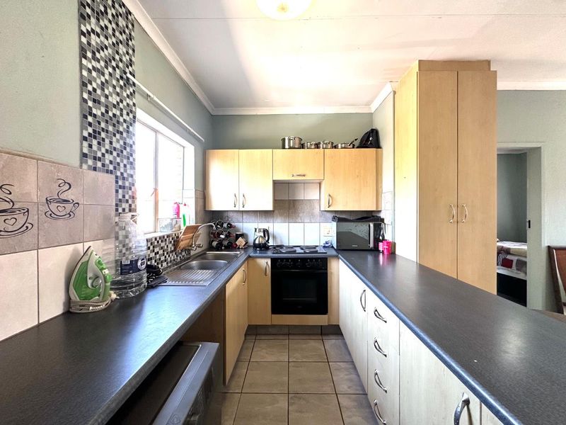 Functional kitchen featuring light wood cabinetry, dark laminate countertops, built-in oven, electric hob, and tiled flooring with a practical U-shaped layout.