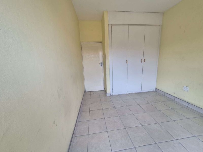 An empty bedroom featuring tiled flooring and a built-in wardrobe, requiring cosmetic updates to the wall finishes.