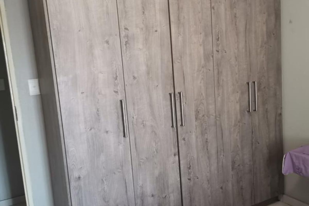 A bedroom featuring a large, modern built-in wardrobe with a wood-grain finish and sleek metal handles.