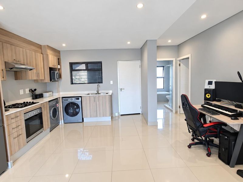 Modern open-plan kitchen featuring light wood cabinetry, integrated appliances, and sleek tiled flooring, seamlessly flowing into a versatile living or workspace area.
