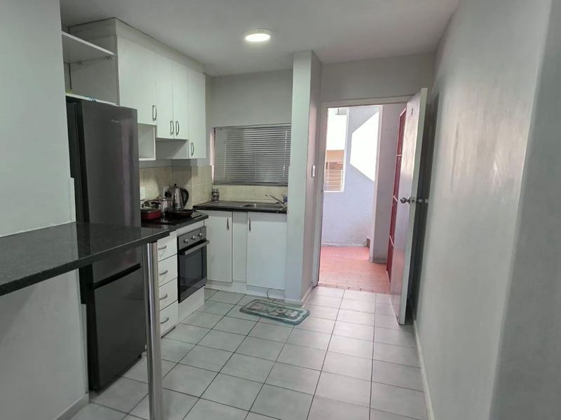 Compact kitchen featuring built-in cabinetry, granite countertops, integrated oven and hob, and tiled flooring with direct access to an outdoor area.