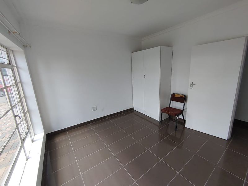 A bright, empty bedroom featuring neutral tiled flooring, a built-in wardrobe, and large windows providing natural light.