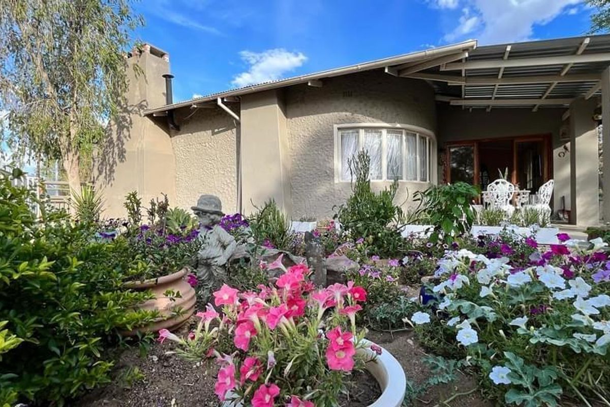 A view of the rear exterior of the house featuring a covered patio area and a well-established garden with flower beds.