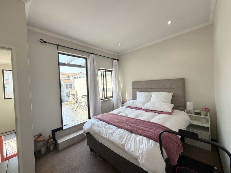 A well-lit bedroom featuring carpeted flooring, recessed downlights, and direct access to a private balcony through a sliding glass door.